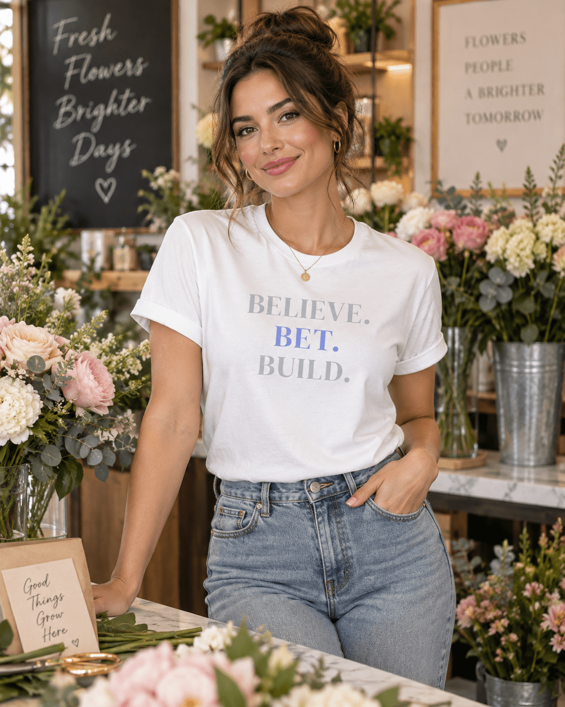 Woman wearing a White Bootstrappin’ BELIEVE. BET. BUILD. founder tee in a flower shop
