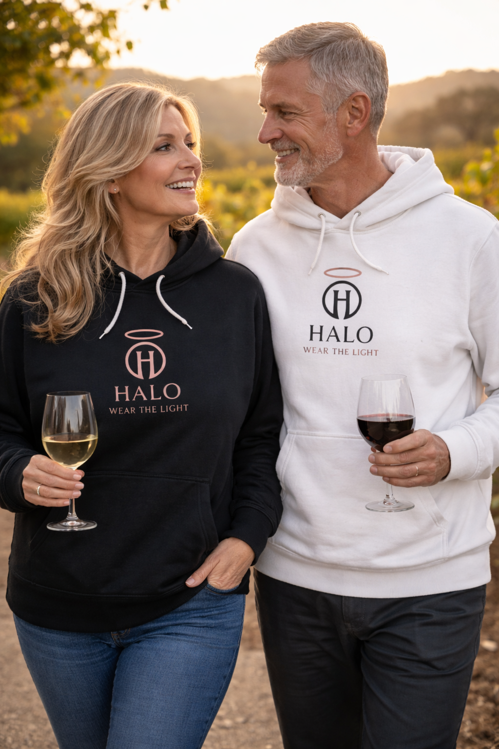 Two people wearing Halo sweatshirts, both holding a glasses of wine, standing outdoors wine venue
