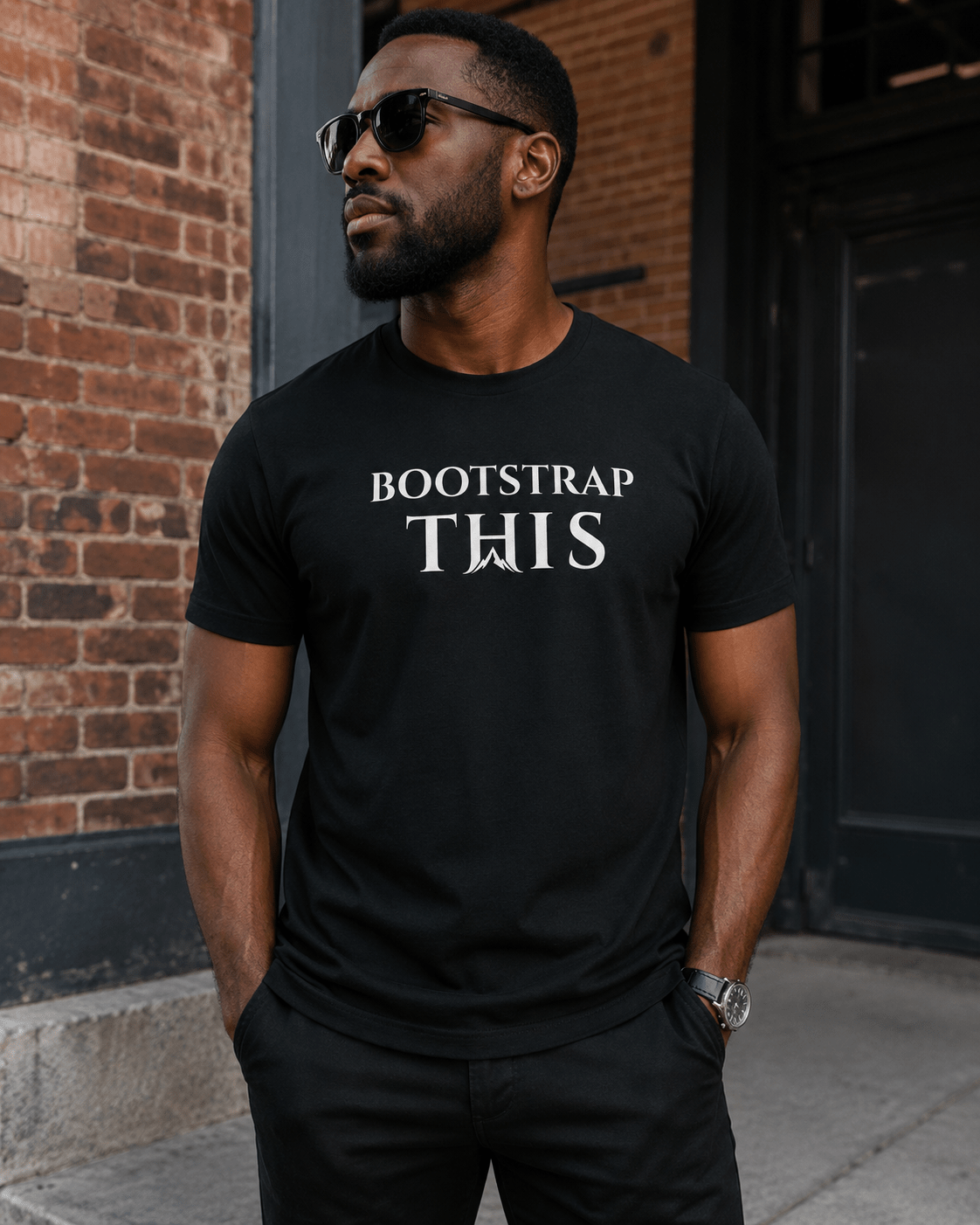 Bootstrap This Men's Tee — White Edition, model wearing the Vintage Black tee by a brick building.