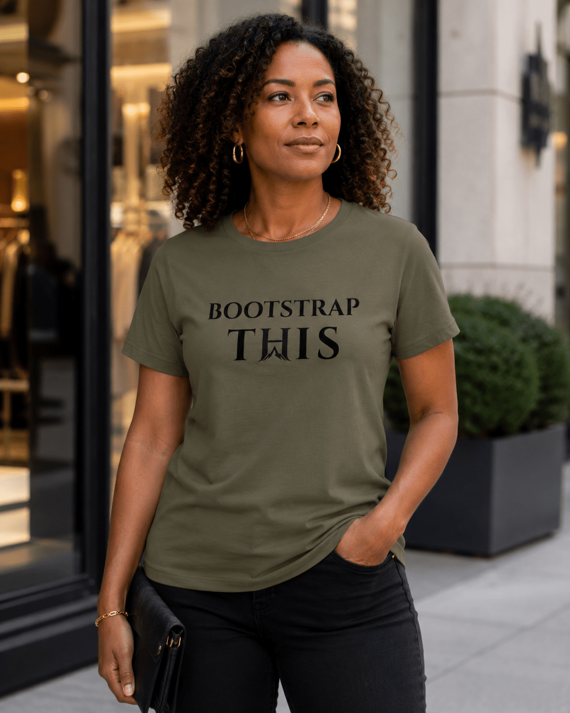Woman wearing the Military Green Bootstrap This Women’s Relaxed Tee with black artwork outside a storefront