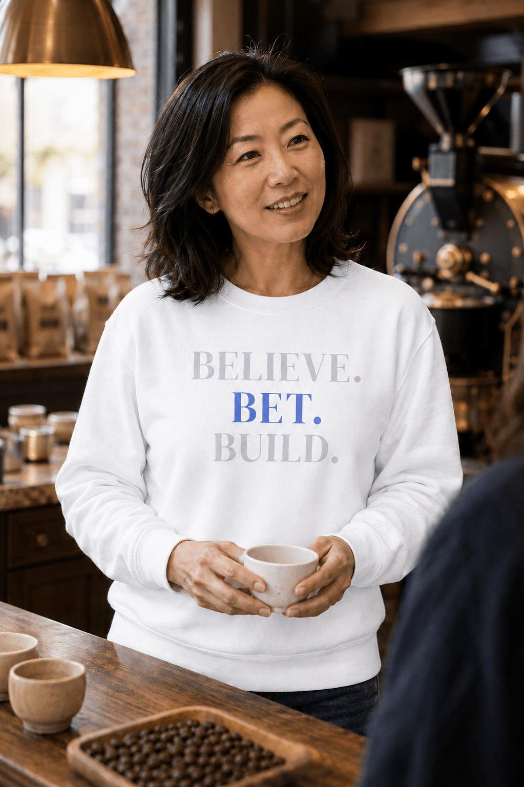 White Bootstrappin’ BELIEVE. BET. BUILD. crewneck — model in a cafe