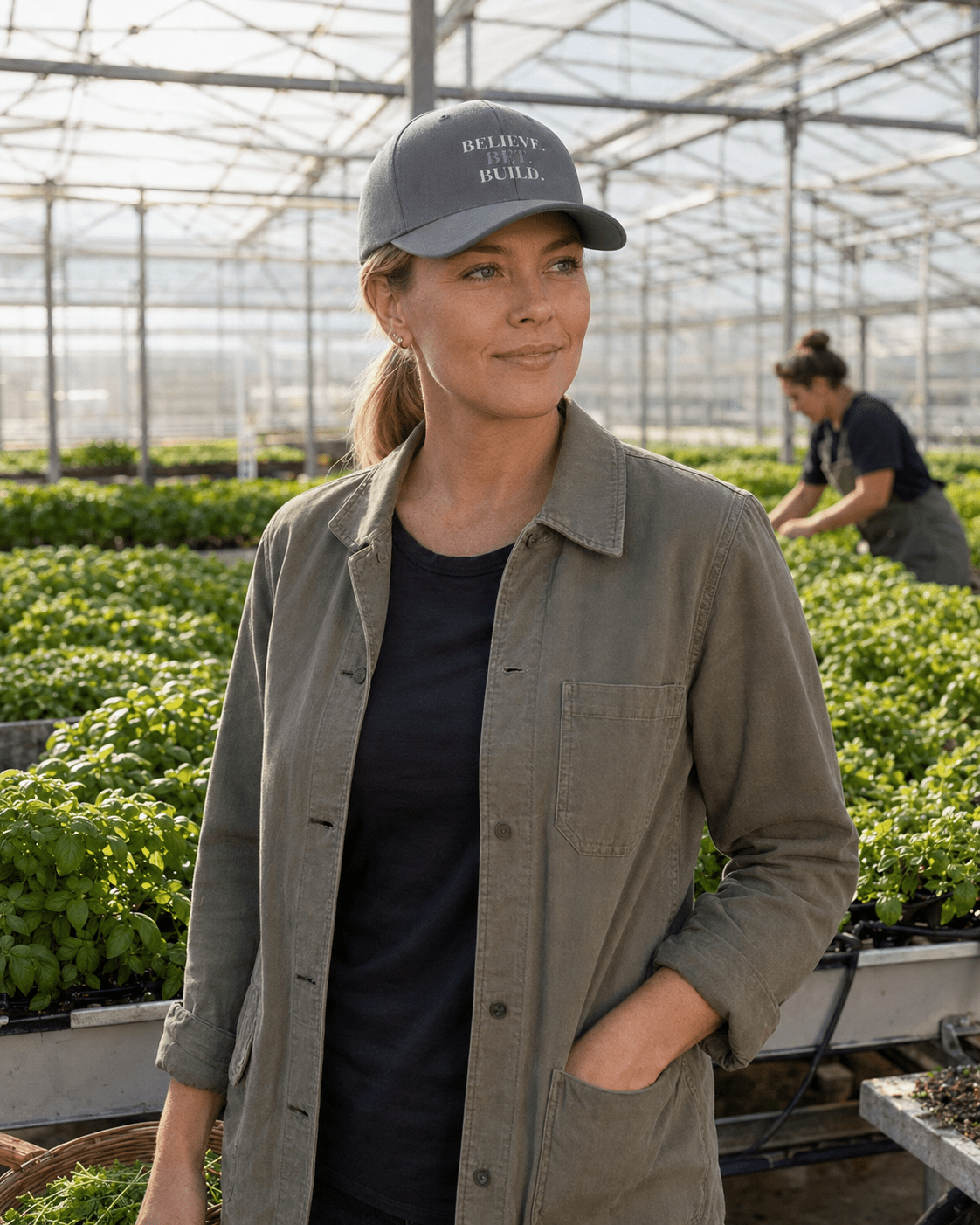 Grey Bootstrappin’ BELIEVE. BET. BUILD. Flexfit cap — model in a greenhouse