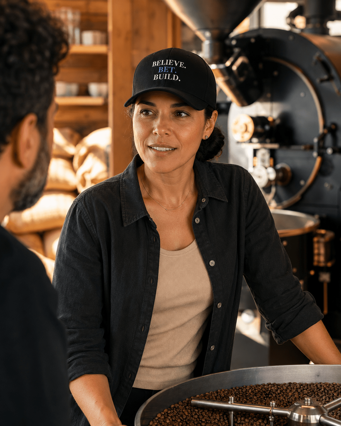 Black Bootstrappin’ BELIEVE. BET. BUILD. Flexfit cap — model in a workshop
