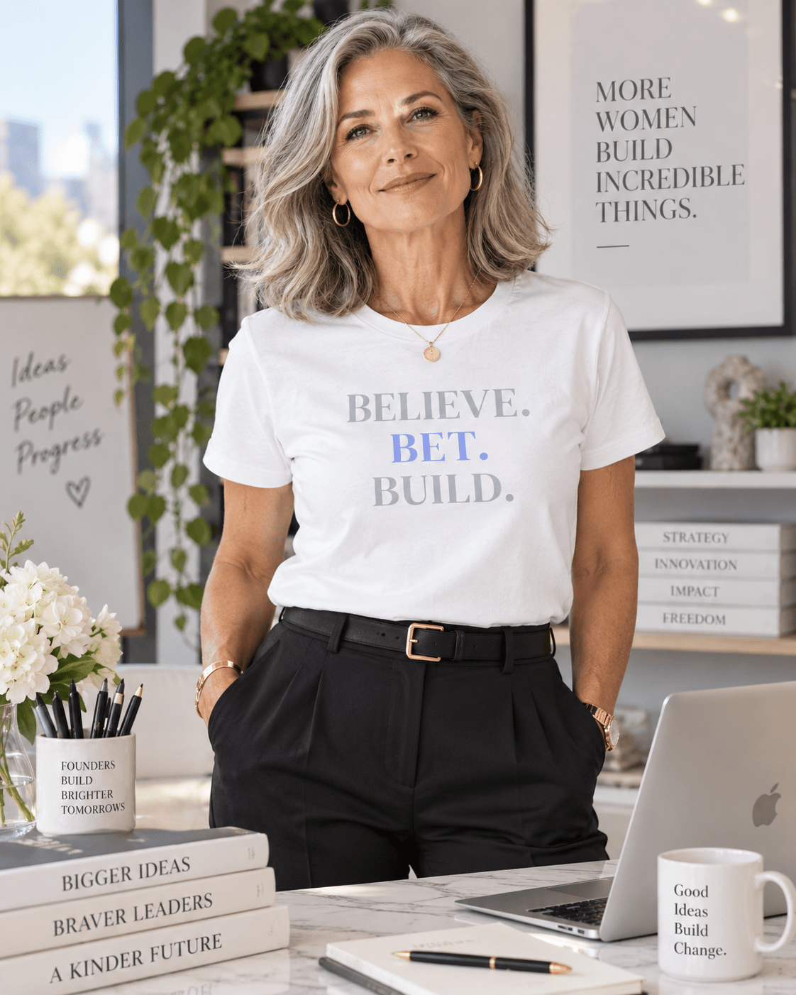 Woman wearing a White Bootstrappin’ BELIEVE. BET. BUILD. founder tee behind an office desk