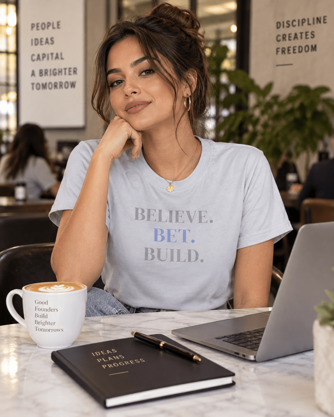Woman wearing a Light Blue Bootstrappin’ BELIEVE. BET. BUILD. founder tee seated at a laptop