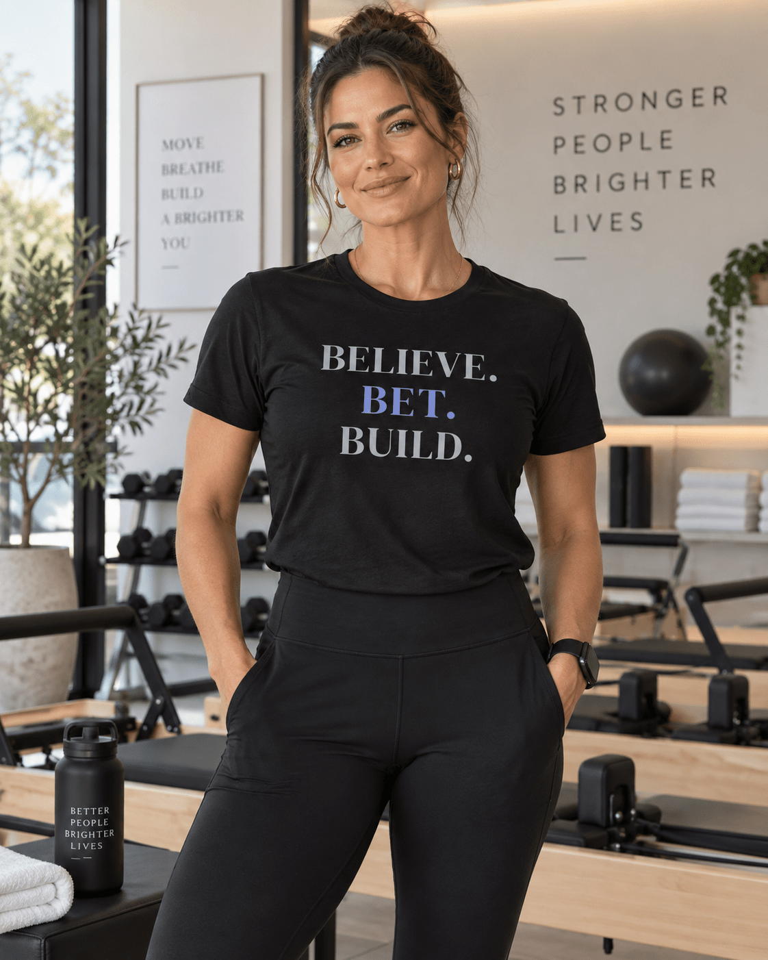 Woman wearing a Black Bootstrappin’ BELIEVE. BET. BUILD. founder tee in an office — front view