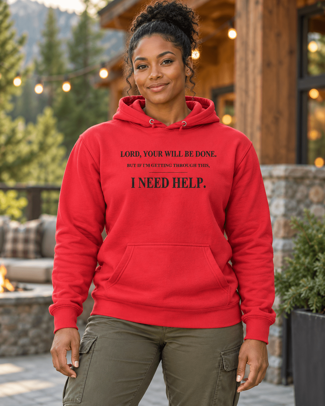 Woman on a lodge patio wearing a Team Red DESCENT faith hoodie, front view showing Your Will Be Done and I Need Help lettering