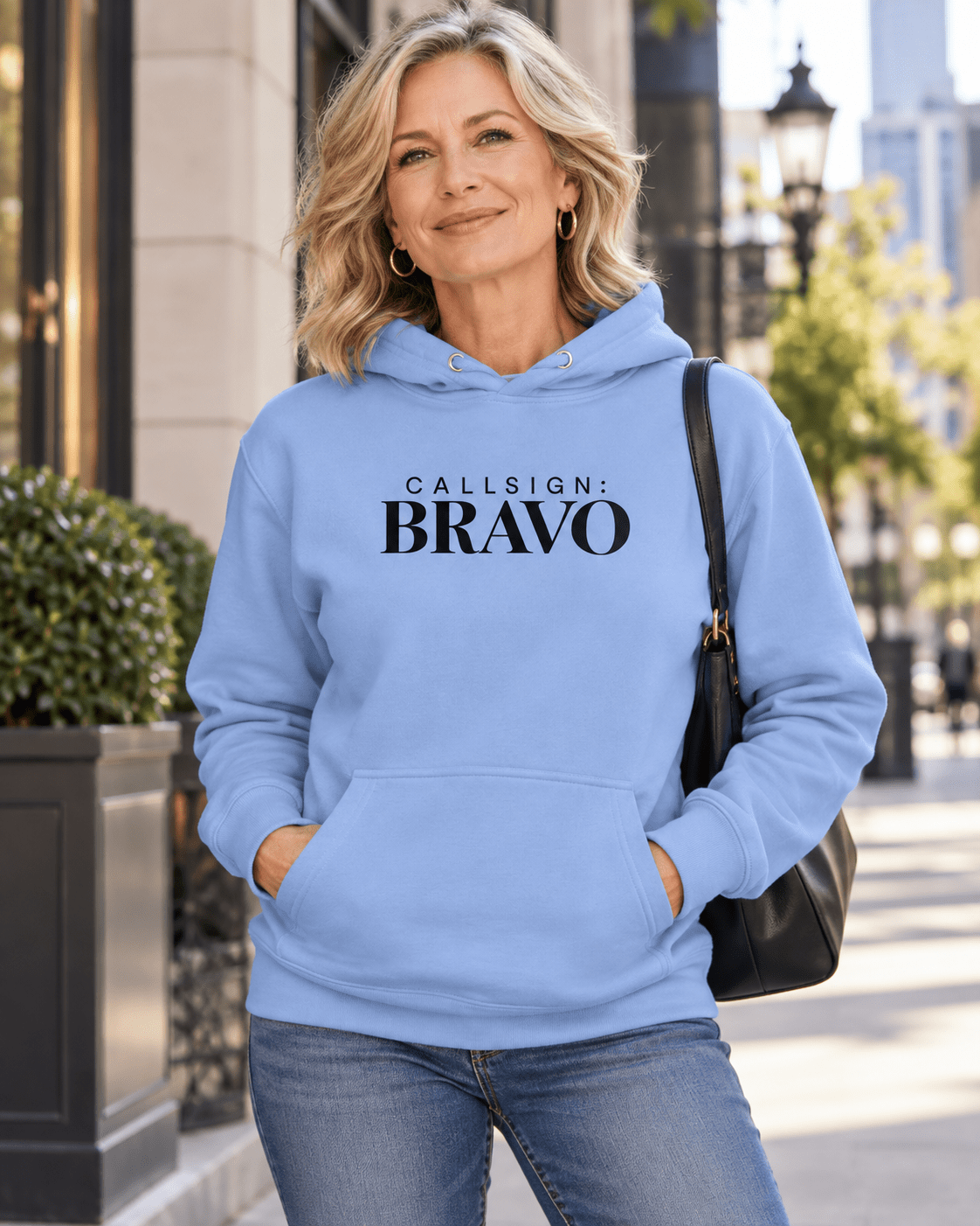 Woman wearing a Carolina Blue God Is Good CALLSIGN: BRAVO hoodie outside a city storefront — front view
