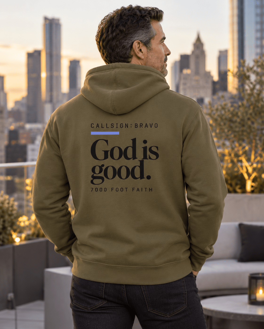 Man wearing a Military Green God Is Good CALLSIGN: BRAVO hoodie on a rooftop terrace — back view