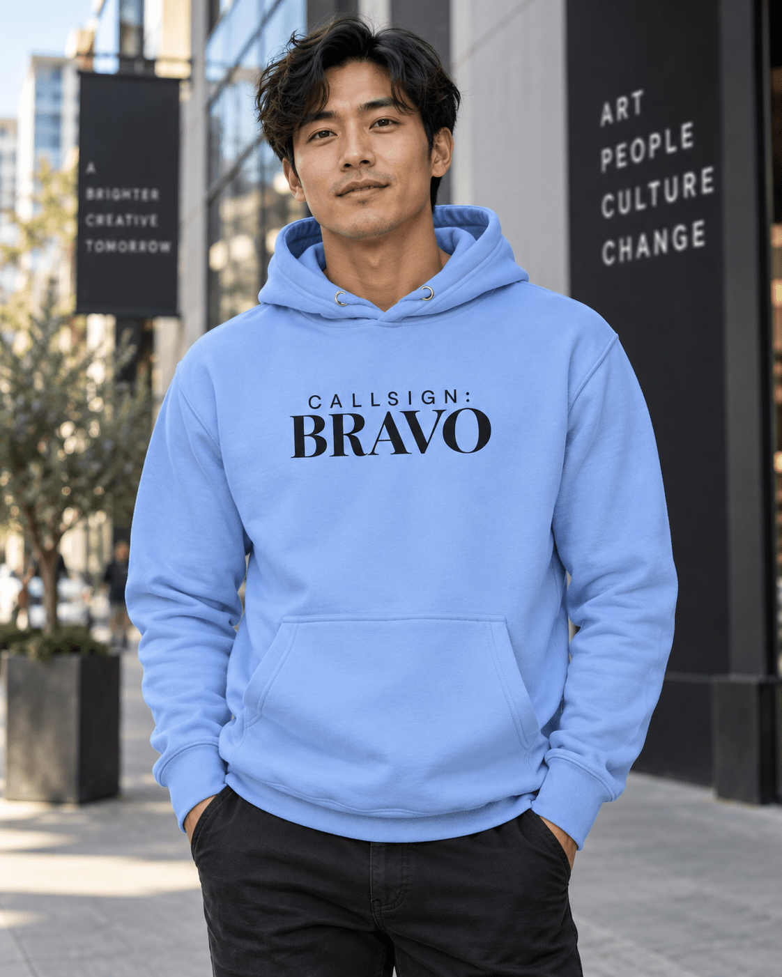 Man wearing a Carolina Blue God Is Good CALLSIGN: BRAVO hoodie outside an art gallery — front view