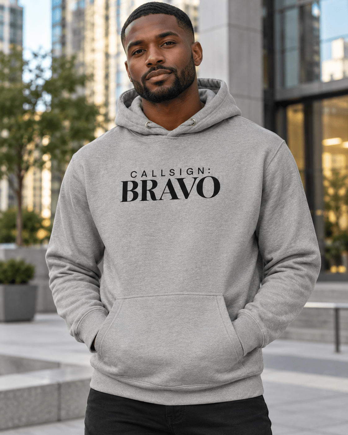 Man wearing a Carbon Grey God Is Good CALLSIGN: BRAVO hoodie in an urban plaza — front view