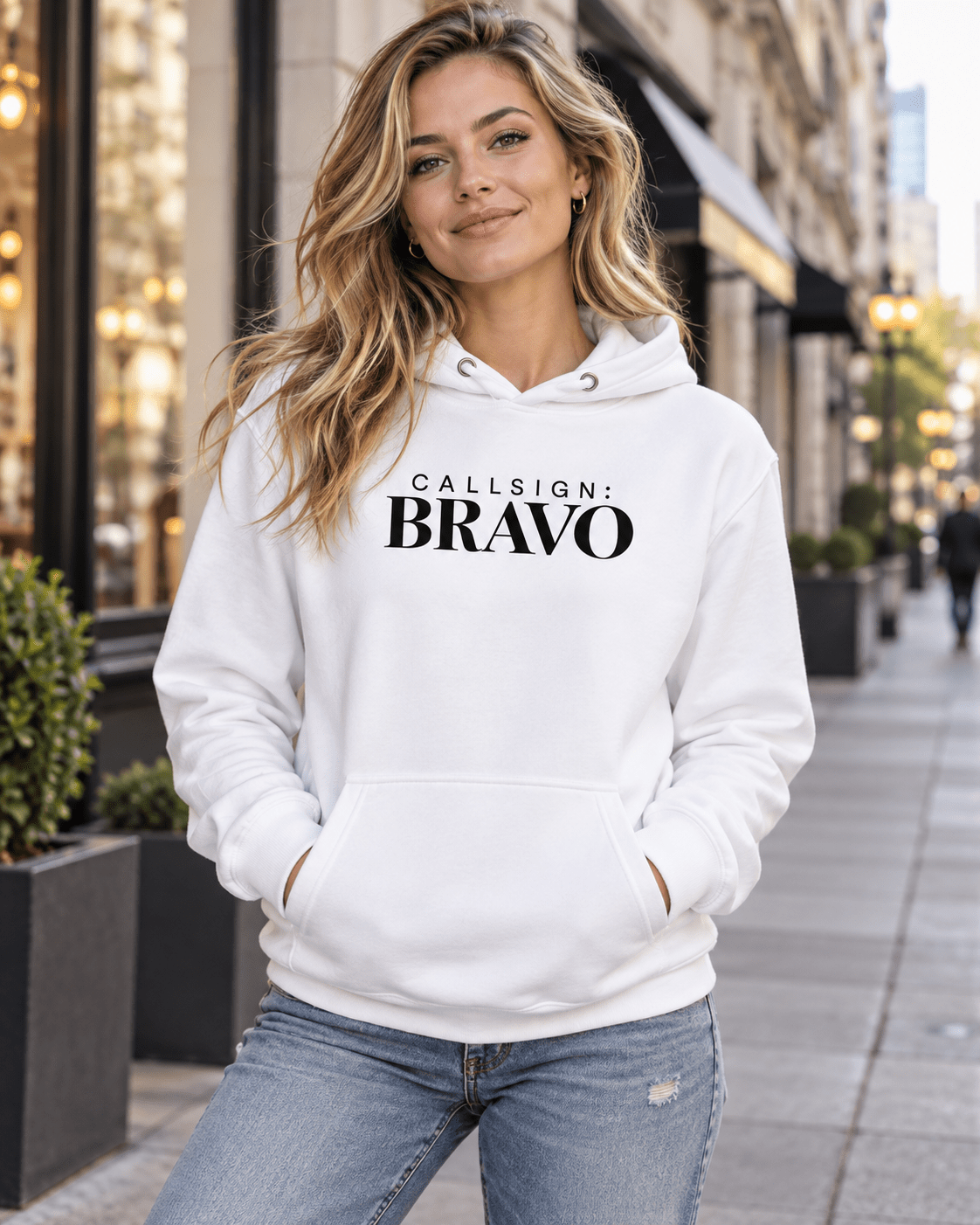 Woman wearing a White God Is Good CALLSIGN: BRAVO hoodie on a city sidewalk — front view