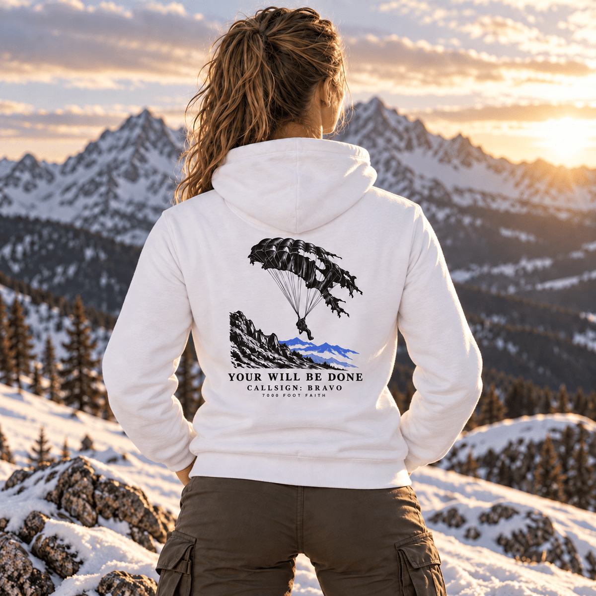 Woman wearing a White Your Will Be Done: Descent CALLSIGN: BRAVO hoodie in snowy mountains — back view