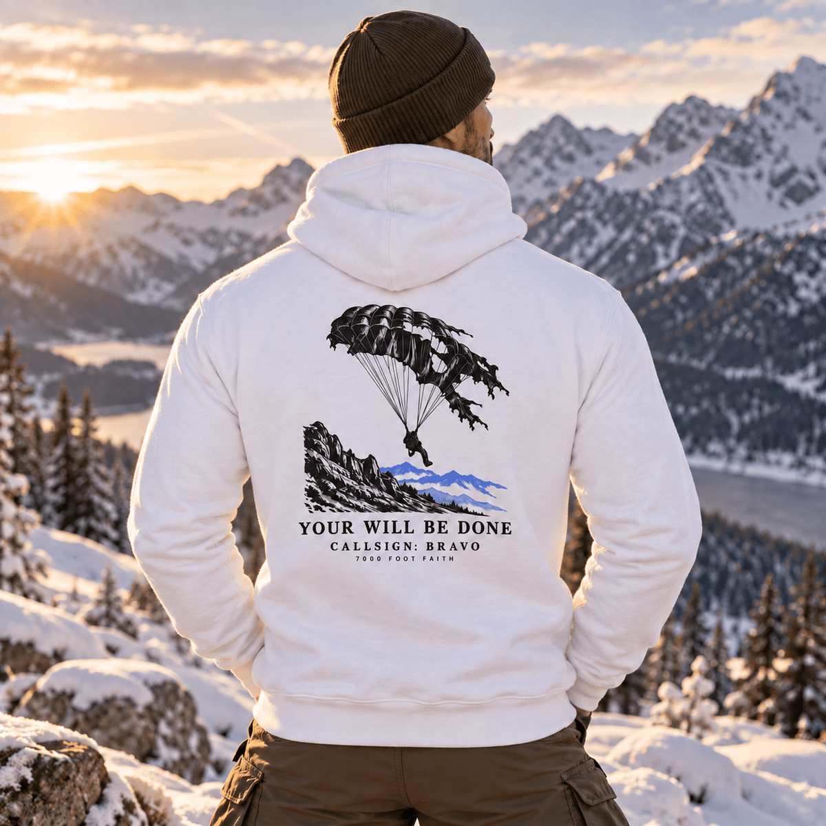 Man wearing a White Your Will Be Done: Descent CALLSIGN: BRAVO hoodie in snowy mountains — back view
