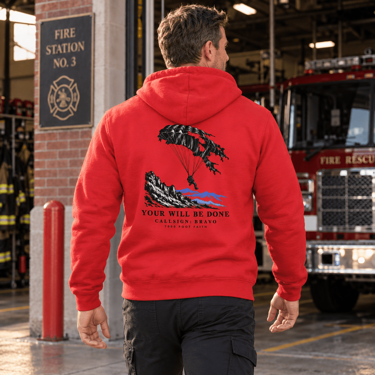Man wearing a Team Red Your Will Be Done: Descent CALLSIGN: BRAVO hoodie outside a fire station — back view