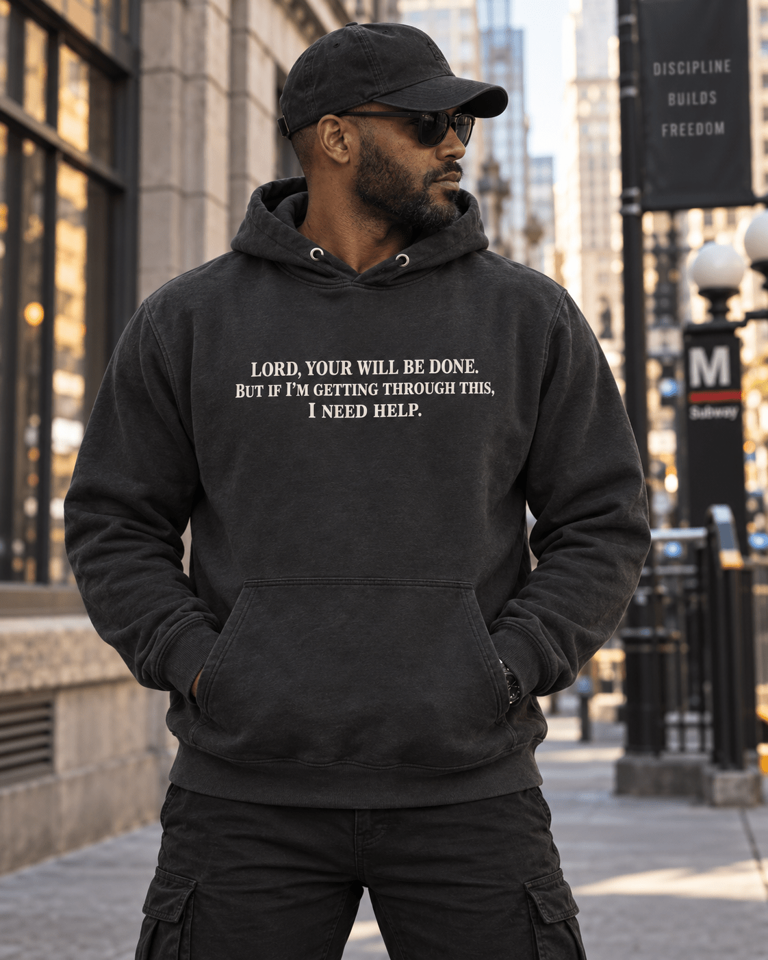 Man wearing a Vintage Black Your Will Be Done: Descent CALLSIGN: BRAVO hoodie on a city sidewalk — front view