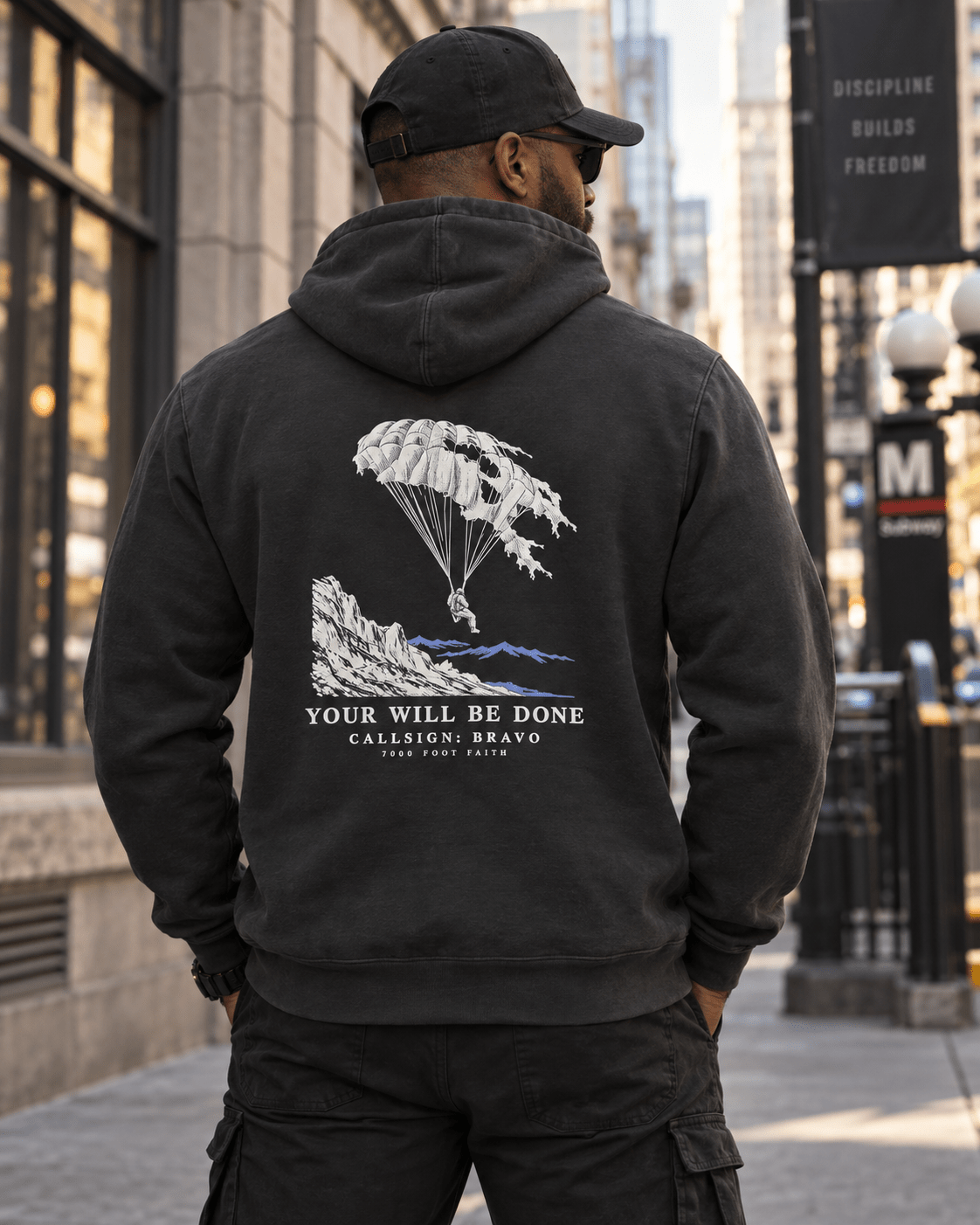 Man wearing a Vintage Black Your Will Be Done: Descent CALLSIGN: BRAVO hoodie on a city sidewalk — back view