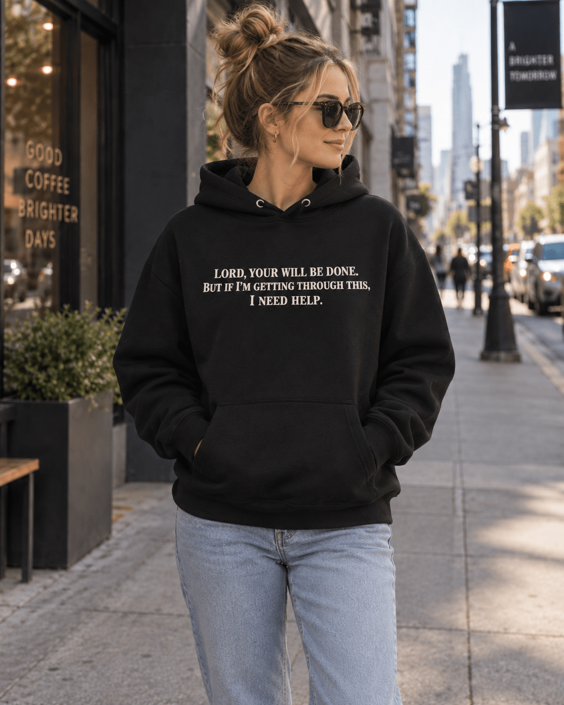 Woman wearing a Black Your Will Be Done: Descent CALLSIGN: BRAVO hoodie outside a city cafe — front view