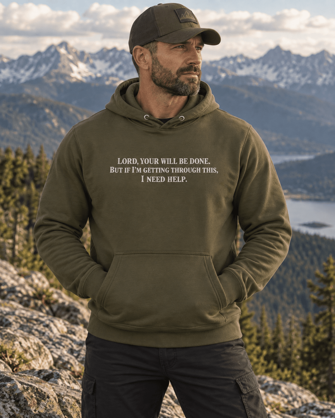 Man wearing a Military Green Your Will Be Done: Descent CALLSIGN: BRAVO hoodie above a mountain lake — front view
