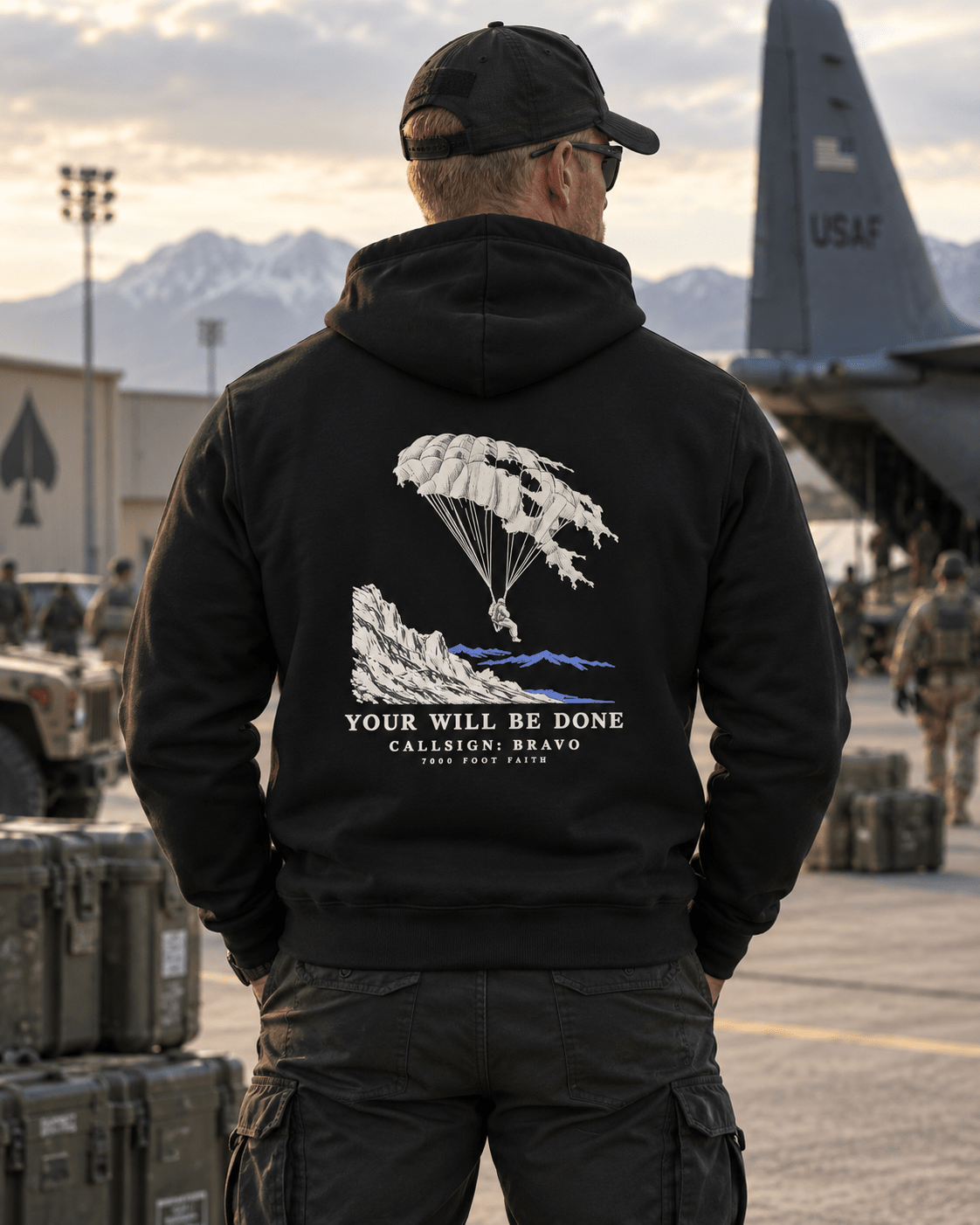 Man wearing a Black Your Will Be Done: Descent CALLSIGN: BRAVO hoodie on an airfield — back view
