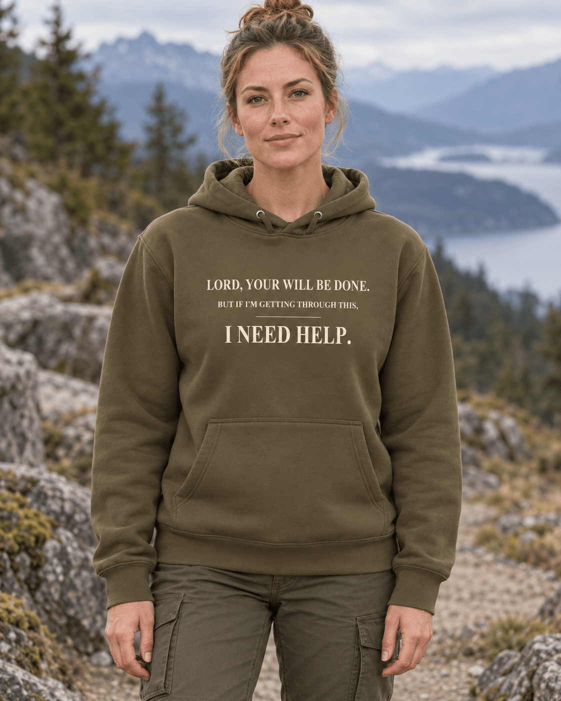 Woman outdoors wearing a Military Green DESCENT faith hoodie, front view showing Your Will Be Done and I Need Help lettering