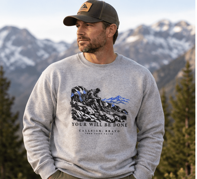 Man wearing a Carbon Grey Your Will Be Done: The Aftermath CALLSIGN: BRAVO crewneck in the mountains — front view