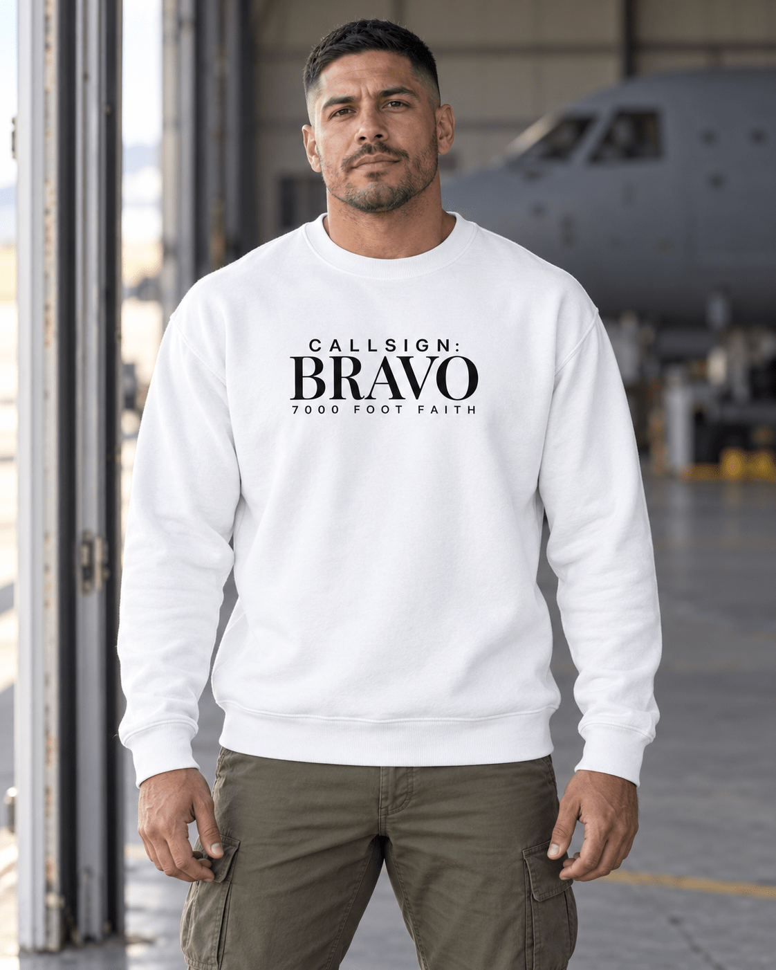 White Zagros Ridgeline CALLSIGN: BRAVO crewneck — male model near a hangar, front view