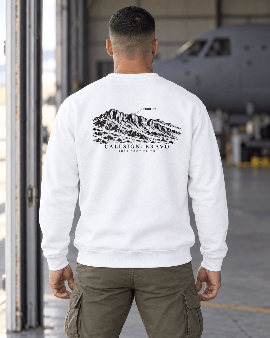 White Zagros Ridgeline CALLSIGN: BRAVO crewneck — male model near a hangar, back view